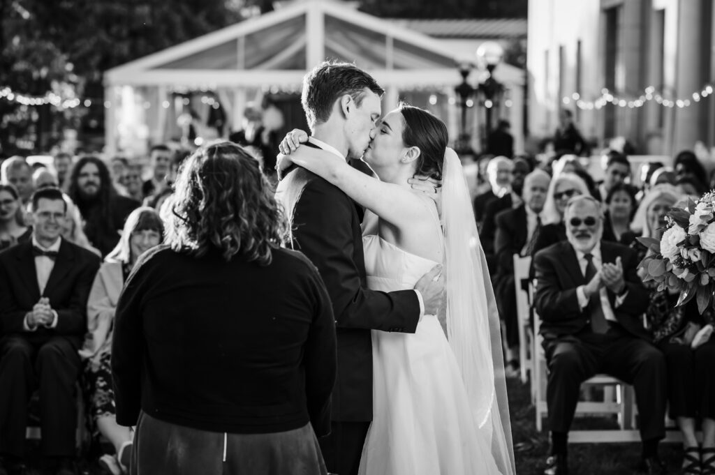 Couple having their first kiss with guests in the background at American Swedish Historical
