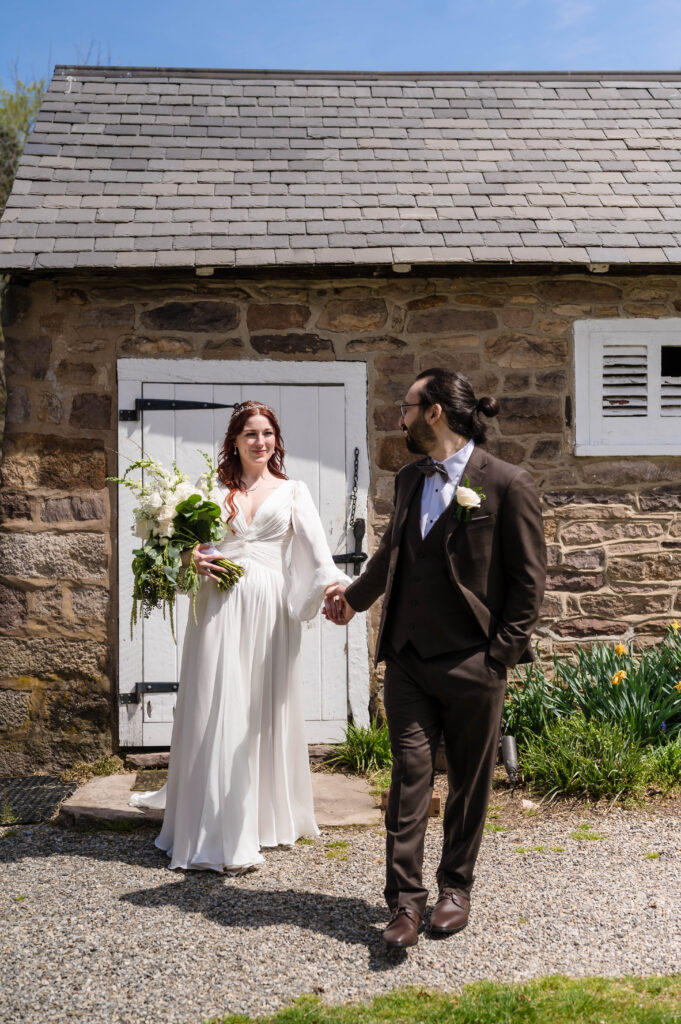 groom leading the bride by the hand outside stone cottage at woolverton inn