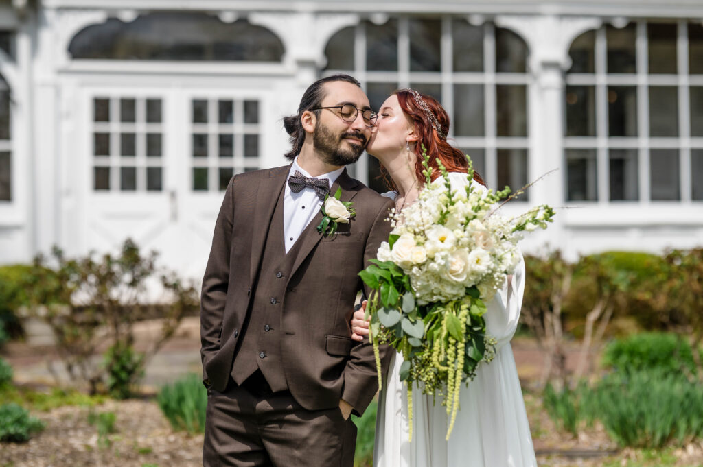 bride kissing groom on the cheek outside woolverton inn